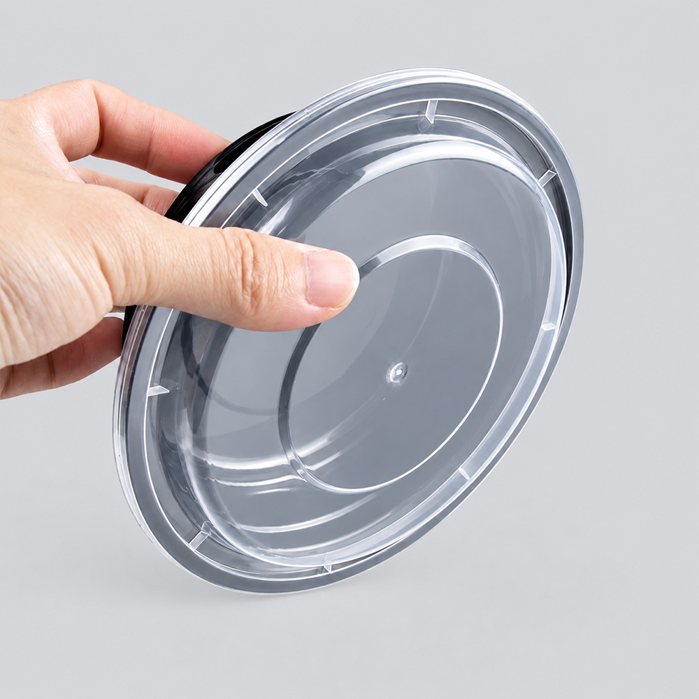 Hand holding a round black container with clear lid