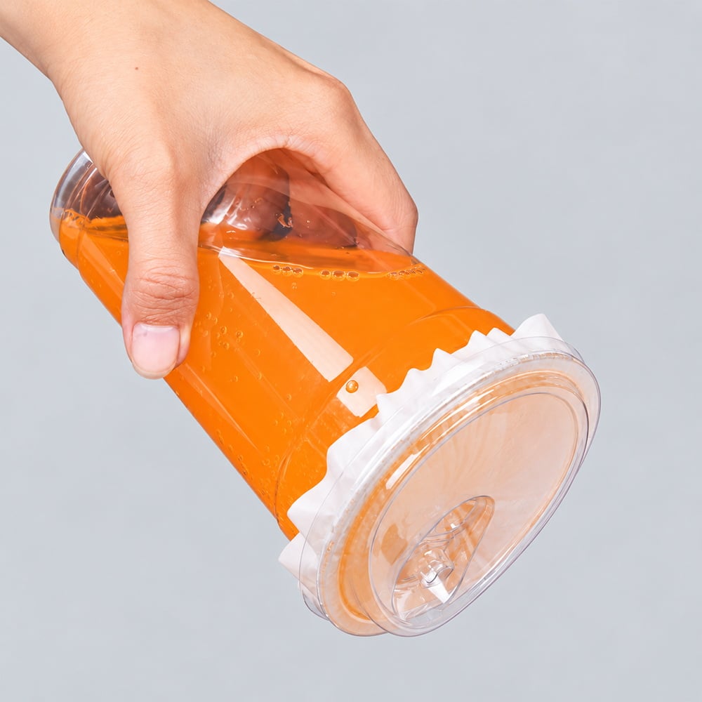 Hand holding clear PET cup of orange drink, lid sealed upside down